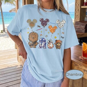 May include: Light blue t-shirt featuring cartoon characters from Star Wars and Mickey Mouse balloons. The design includes Chewbacca, R2-D2, BB-8, and an Ewok. The word "Chambray" is printed on the bottom right of the shirt.