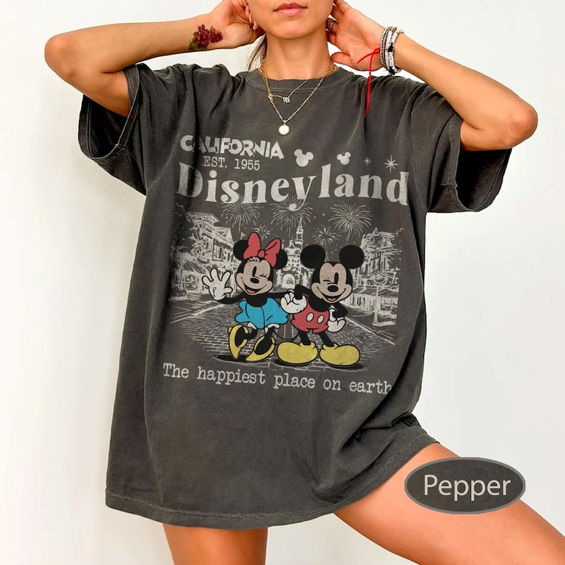 May include: Dark gray t-shirt featuring a graphic of Mickey and Minnie Mouse in front of Disneyland. The shirt has the text "CALIFORNIA EST. 1955 Disneyland" and "The happiest place on earth."
