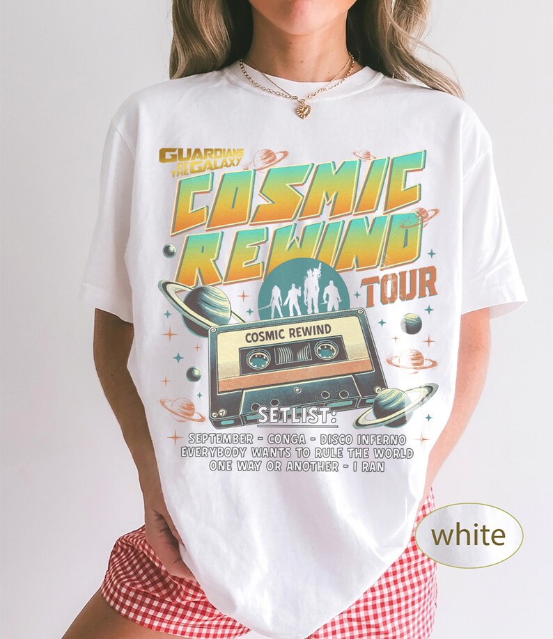 K&ouml;nnte beinhalten: Wei&szlig;es T-Shirt mit Retro-Design. Das Shirt zeigt den Text "COSMIC REWIND TOUR" und eine Kassettenband-Grafik. Das Design beinhaltet Planeten und Sterne sowie eine Setlist mit Songtiteln.