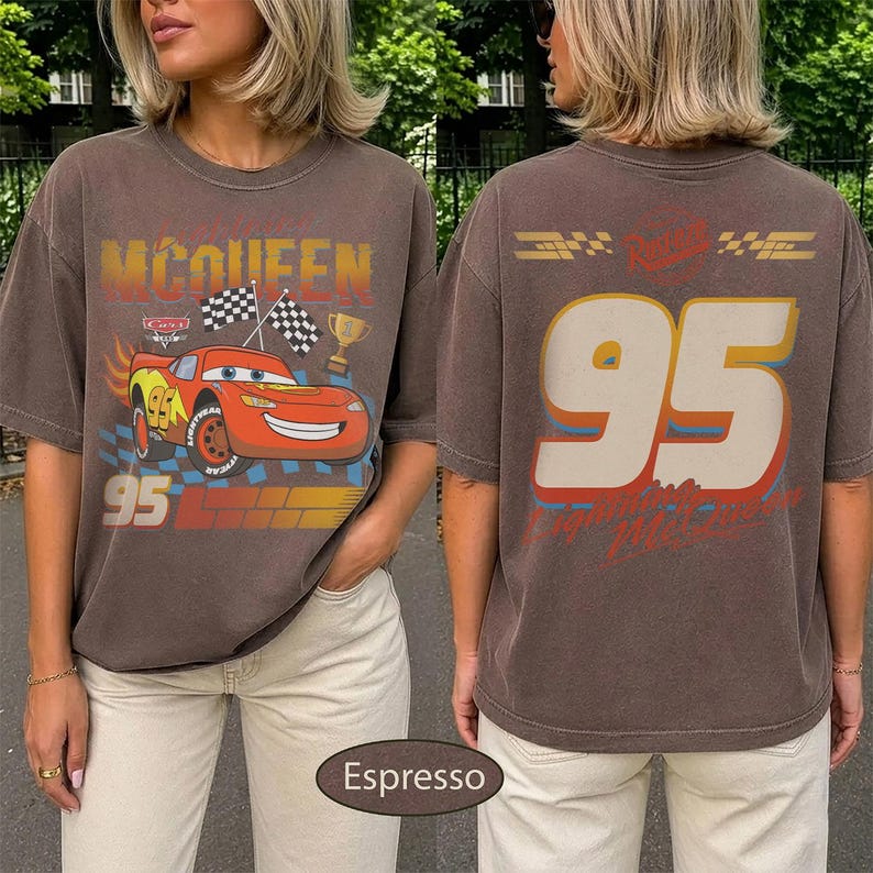 May include: Espresso-colored t-shirt featuring a graphic of a red race car with the number 95 and the name "McQueen". The front design includes checkered flags and a trophy. The back displays the number 95 in large, off-white letters.