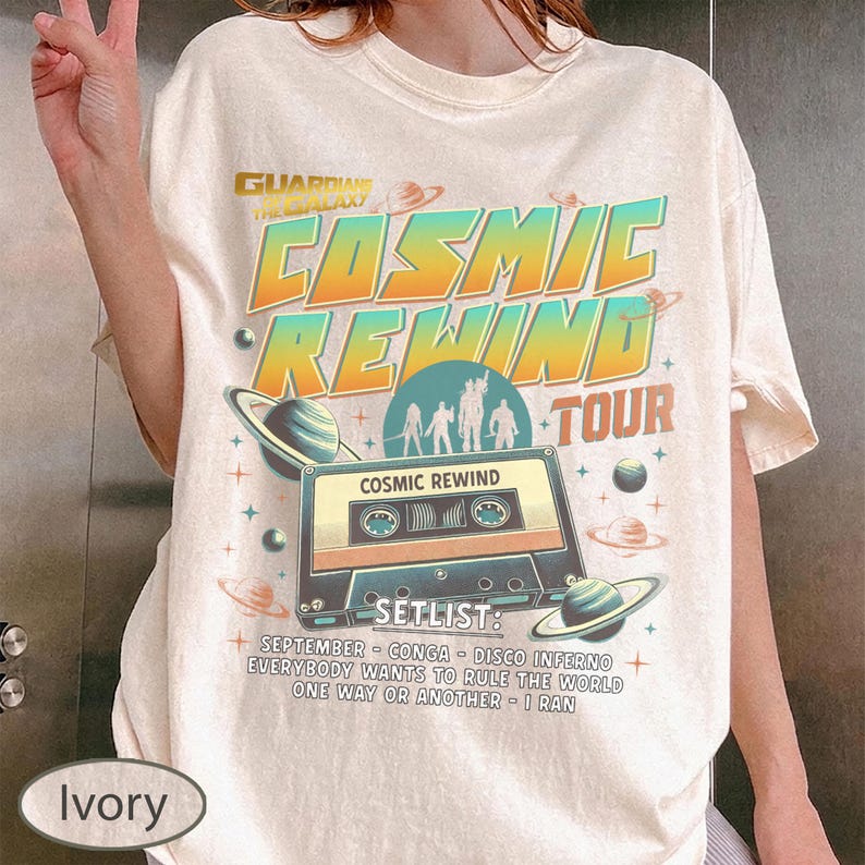 K&ouml;nnte beinhalten: Elfenbeinfarbenes T-Shirt mit dem Text "Guardians of the Galaxy Cosmic Rewind Tour" in Orange und T&uuml;rkis. Das Design zeigt eine Kassette, Planeten und die Setlist: September, Conga, Disco Inferno, Everybody Wants to Rule the World, One Way or Another, I Ran.