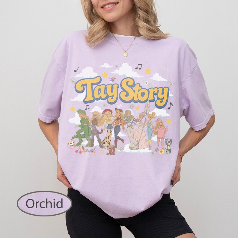 K&ouml;nnte beinhalten: Ein orchideefarbenes T-Shirt mit dem gelben Schriftzug Tay Story in einer Retro-Schriftart. Die Grafik zeigt eine Gruppe illustrierter Figuren in verschiedenen Outfits, umgeben von wei&szlig;en Wolken, gelben Sternen und schwarzen Noten auf hellem Grund.