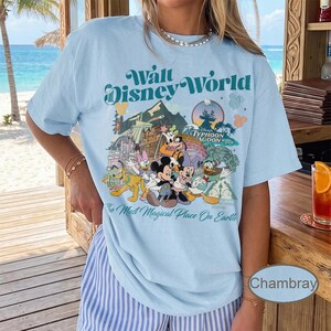 May include: Light blue t-shirt featuring a vintage-style graphic of Walt Disney World characters and attractions. The shirt includes the text "Walt Disney World" and "The Most Magical Place On Earth."