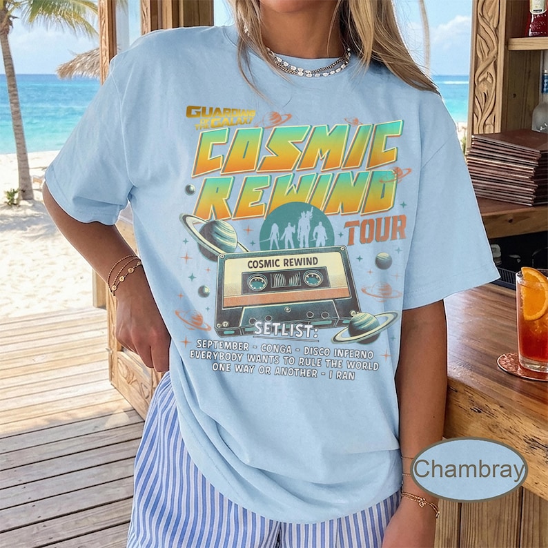 K&ouml;nnte beinhalten: Hellblaues T-Shirt mit einem Grafikdesign, das die "Cosmic Rewind Tour" bewirbt. Das Design zeigt eine Kassette, Planeten und den Text "Cosmic Rewind Tour" in Orange und Gr&uuml;n. Die Setlist enth&auml;lt Songs wie "September" und "Disco Inferno".