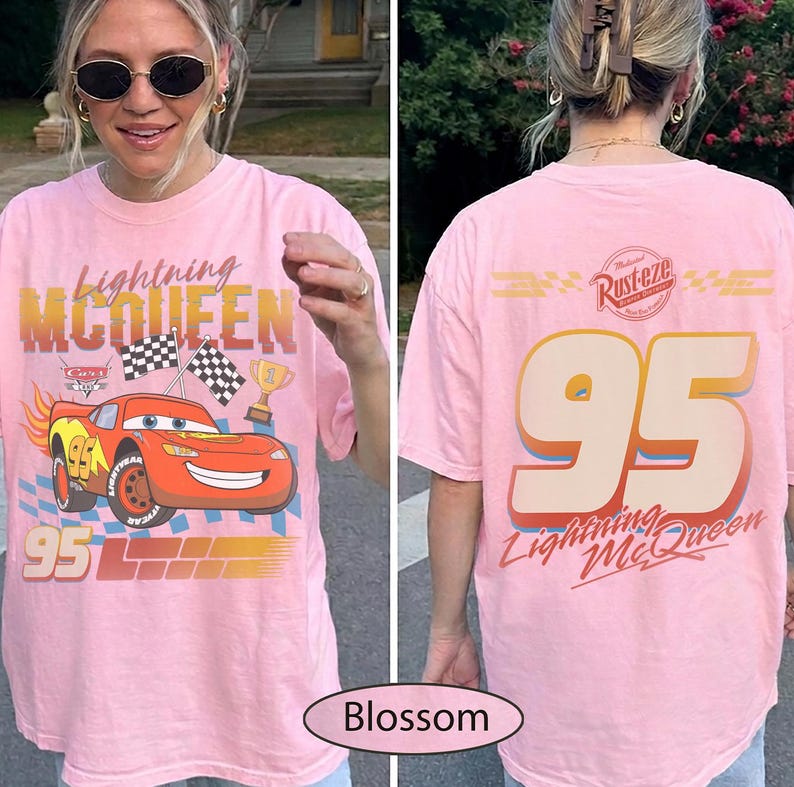 May include: Pink t-shirt featuring a graphic of Lightning McQueen from the Cars movie. The front design includes the text "Lightning McQueen" and "95". The back of the shirt has "95" and "Lightning McQueen" with the Rust-eze logo.