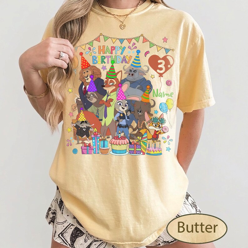 May include: Butter-colored t-shirt featuring a colorful graphic of cartoon animals, party hats, and the text "Happy Birthday 3". The design includes a heart-shaped balloon and the word "Name".
