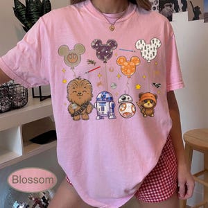 May include: Pink t-shirt featuring Star Wars characters and Mickey Mouse-shaped balloons. The design includes Chewbacca, R2-D2, BB-8, and an Ewok. The word "Blossom" is printed at the bottom of the image.