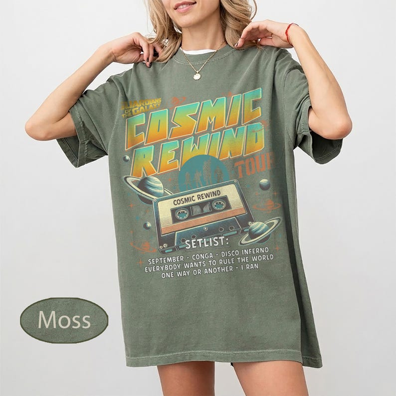 K&ouml;nnte beinhalten: Moosgr&uuml;nes T-Shirt mit Retro-Grafikdesign. Das Design zeigt den Text "COSMIC REWIND TOUR" mit einem Kassettenrekorder und Planeten. Die Setlist enth&auml;lt Songs wie "September" und "One Way or Another".