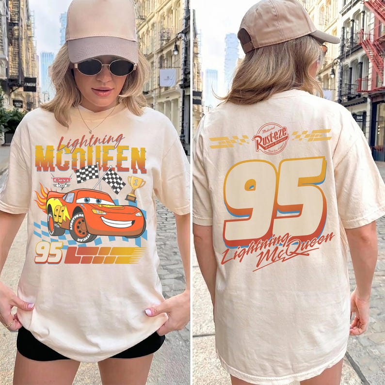 May include: Cream-colored t-shirt featuring Lightning McQueen from the Cars movie. The front graphic shows McQueen with flames, checkered flags, and the number 95. The back displays the number 95 and the text "Lightning McQueen".