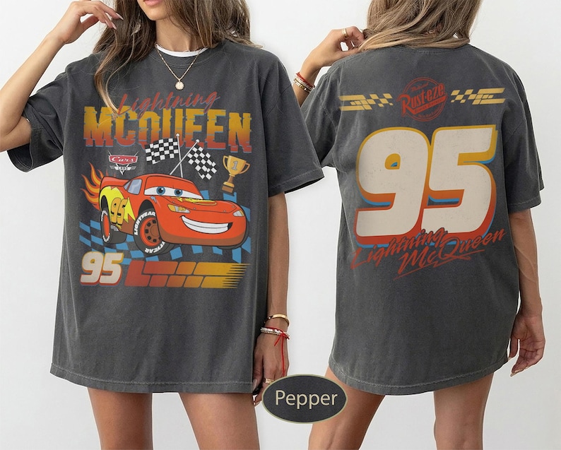 May include: Dark gray t-shirt featuring a graphic of Lightning McQueen from the movie Cars. The front design includes the number 95, checkered flags, and the text "Lightning McQueen". The back of the shirt also displays "95" and "Lightning McQueen".
