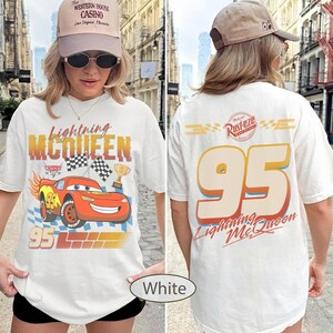 May include: White t-shirt featuring Lightning McQueen from the Cars movie. The front graphic includes the character, the number 95, and the text "Lightning McQueen". The back displays "95" and "Lightning McQueen".