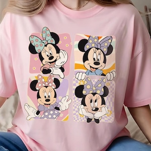 May include: Pink t-shirt featuring a four-panel graphic of Minnie Mouse in various poses. Each panel showcases a different Minnie Mouse design with polka dot bows and backgrounds in pastel colors.