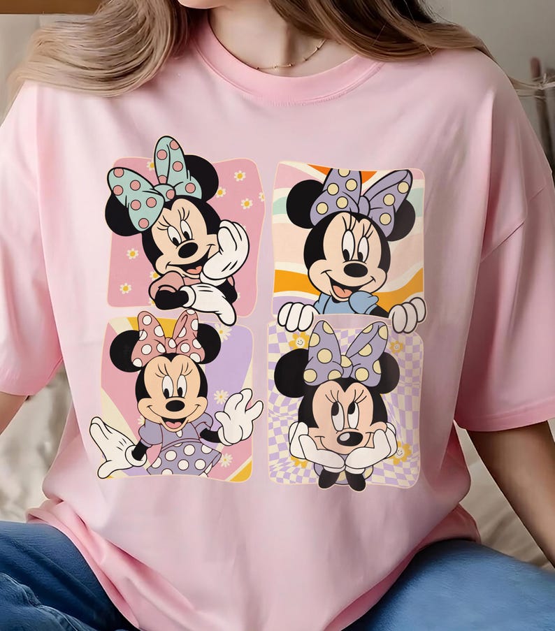 May include: Pink t-shirt featuring a four-panel graphic of Minnie Mouse in various poses. Each panel showcases a different Minnie Mouse design with polka dot bows and backgrounds in pastel colors.