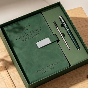 May include: A dark green notebook set in a matching box, featuring a silver magnetic clasp. The cover is engraved with "The OFFICIANT ALBERT WHITE" and "ASHLEY & BENJAMIN JULY 17, 2027". Includes a dark green pen and a thin silver metal stylus.