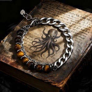 May include: A silver chain bracelet with tiger eye beads. The bracelet features a curb chain and a strand of polished, round tiger eye beads. The bracelet is displayed on a vintage book with an octopus illustration.