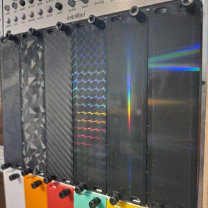 Puede incluir: Paneles de sintetizador modular con diversos diseños texturizados y holográficos. Los paneles negros presentan patrones geométricos, fibra de carbono y efectos de arcoíris iridiscentes. Montados en un marco metálico.