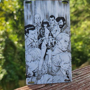 May include: Black and white engraved metal plate featuring a group of characters from a manga or anime. The characters are drawn in a realistic style and appear to be in a dramatic scene.