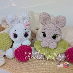 May include: Two plush crochet bunnies, one white with a pink bow and one grey, sit with decorative eggs. The bunnies have large eyes and are holding a red ball. The text "LOW SEW crochet pattern" is visible.