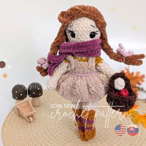 May include: A plush crochet doll with brown yarn hair in braids, wearing a purple scarf, a light beige dress, and patterned socks. The doll holds a dark brown basket containing red apples. Text on the image reads: SNOWFOXCROCHET LOW SEW crochet pattern.