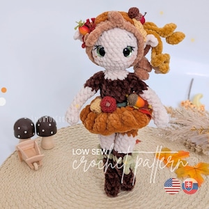 Puede incluir: Una muñeca de ganchillo con cara color crema, grandes ojos verdes y un conjunto marrón texturizado. La muñeca lleva un gorro adornado con pequeñas bayas rojas y naranjas y hojas. El texto "LOW SEW crochet pattern" es visible en la imagen.