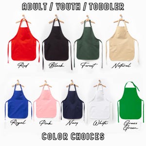 May include: A selection of aprons in a range of colours: red, black, forest green, natural, royal blue, pink, navy, white, and grass green. Each apron is displayed on a wooden hanger. Text at the top reads "ADULT / YOUTH / TODDLER" and "COLOR CHOICES" at the bottom.