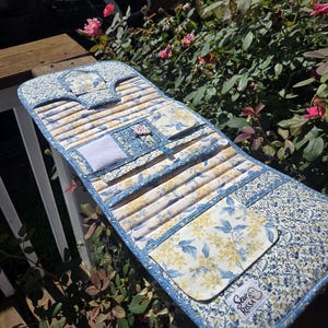 May include: A fabric organizer roll featuring a blue and white floral pattern with yellow accents. It includes multiple stitched slots, a small square pocket, a white velcro patch, and a label with the text Sew RISSA in the bottom corner.