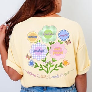 May include: A light yellow t-shirt with a floral design on the back. The design features flowers with the words "strategy", "writers", "support", "specialized", and "self paced". The text "helping little minds grow" is also included.