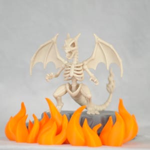 May include: A skeletal dragon figurine with outstretched wings and a fiery base. The dragon is off-white, with detailed bone structure. The flames are bright orange, creating a striking contrast against the neutral background.