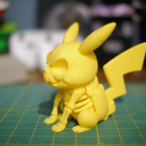 Może przedstawiać: Żółta figurka Pikachu z motywem szkieletu. Figurka ma ogon w kształcie błyskawicy i spiczaste uszy. Figurka siedzi na zielonej powierzchni z siatką.