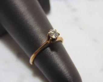 May include: A gold ring with a single round diamond set in a prong setting.
