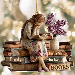 Könnte beinhalten: Dekorative Verzierung, die eine lesende Frau zeigt, die auf Büchern sitzt. Die Frau trägt ein Blumenkleid und hat lange braune Haare. Die Verzierung enthält den Text "Emily" und "Just a Girl who loves BOOKS."