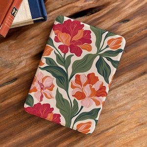 Könnte beinhalten: Eine rechteckige Hülle mit floralem Muster. Das Design zeigt rote, orangefarbene und rosa Blüten und grüne Blätter auf cremefarbenem Hintergrund. Die Hülle liegt auf einer Holzoberfläche, im Hintergrund ist ein Buch zu sehen.