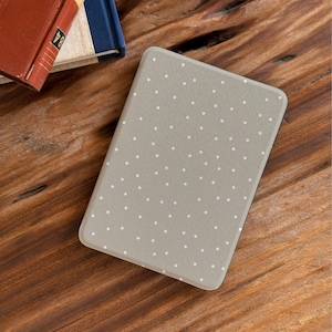 Könnte beinhalten: Eine graue E-Reader-Hülle mit einem weißen Polka-Dot-Muster. Die Hülle ist rechteckig mit abgerundeten Ecken. Im Hintergrund sind Bücher auf einer Holzoberfläche zu sehen.