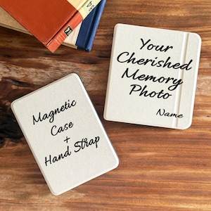 Puede incluir: Dos fundas magnéticas blanquecinas con texto negro. Una dice "Magnetic Case + Hand Strap", la otra "Your Cherished Memory Photo" con espacio para un nombre. Libros en el fondo.