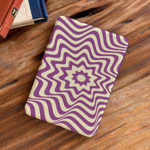 May include: A rectangular case with a purple and cream-colored wavy starburst pattern. The case is on a wooden surface, with a glimpse of a book in the background.