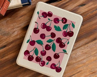 May include: A rectangular e-reader device with a cream-colored frame and a screen displaying a repeating pattern of dark red cherries with green stems and leaves set against a soft pink rectangular background on the display surface.