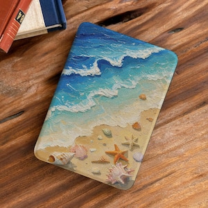 May include: A rectangular e-reader cover featuring a textured, impasto-style painting of a beach scene. The design displays blue ocean waves washing onto a sandy shore decorated with various seashells and a prominent orange starfish.