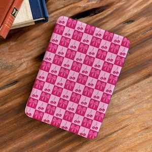 Puede incluir: Una funda rectangular para lector electrónico con un patrón de tablero de ajedrez repetitivo en tonos alternos de rosa claro y oscuro. El diseño incluye pequeñas ilustraciones de cerezas rojas y lazos rosas centradas en cada cuadrado.