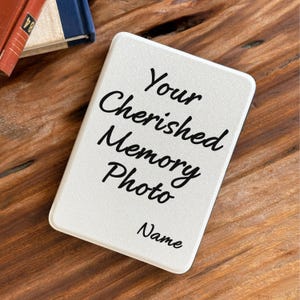 Könnte beinhalten: Eine rechteckige weiße Platte mit abgerundeten Ecken, die den schwarzen Aufdruck Your Cherished Memory Photo und das Wort Name darunter trägt. Die Platte hat eine glatte, matte Oberfläche und liegt schräg auf einer Holzoberfläche.