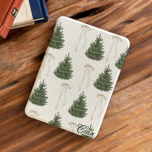 May include: A rectangular e-reader case with a cream-colored background featuring a repeating pattern of green pine trees and light beige ribbons. The name Cian is printed in a dark script font near the bottom right corner of the cover.