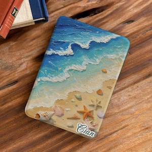 May include: A rectangular tablet case featuring a textured oil painting of a beach scene with blue ocean waves crashing onto a sandy shore. The sand is decorated with various seashells and a starfish, with the name Cian printed in white.