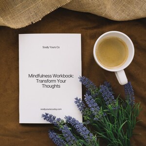 May include: A white workbook titled "Mindfulness Workbook: Transform Your Thoughts" with the text "Soully Yours Co" and "soullyyoursco.etsy.com". A white mug of coffee and a bundle of lavender are also on the brown surface.