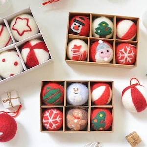 Peut inclure: Plusieurs boîtes de décorations de Noël. Les ornements sont blancs et rouges, avec divers motifs dont une étoile, des rayures, un bonhomme de neige, un sapin de Noël et un flocon de neige. Les ornements sont en feutre.