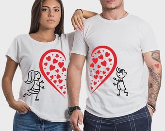 Puede incluir: Dos camisetas blancas con un diseño de corazón rojo. Cada camiseta presenta la mitad de un corazón lleno de corazones rojos y una figura de palo. Las camisetas las llevan dos personas, una con vaqueros azules y la otra con pantalones de cuadros.