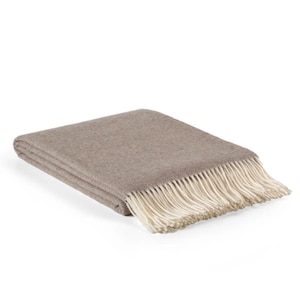 May include: A folded, taupe-colored blanket with a cream-colored fringe. The blanket is made of a soft material and is folded neatly, showcasing its texture and design. The fringe adds a decorative element.