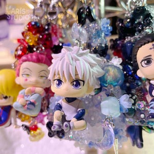 May include: A collection of anime-style character keychains featuring a central figure with spiky white hair and purple eyes, surrounded by various colorful beads, charms, and smaller character figurines in a dense, layered arrangement.