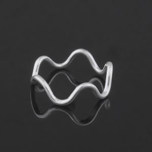 May include: A silver-colored ring with a wavy design. The ring's shape resembles a continuous series of rounded waves. The ring is displayed on a reflective black surface, enhancing its visual appeal. This piece of jewelry is a minimalist accessory.
