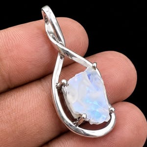 May include: A silver pendant featuring a raw, iridescent moonstone set within a polished, twisted metal frame. The pendant has a teardrop-shaped design with a bail at the top, showcasing the natural, translucent blue and white hues of the stone.
