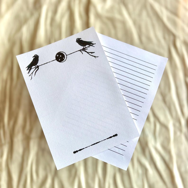 May include: Two sheets of white stationery. One is blank, the other has horizontal lines. Both have a black illustration of two birds on a branch with a moon and stars. A black decorative line is at the bottom.