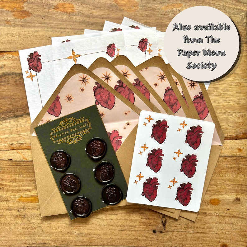 May include: A stationery set with anatomical heart designs. The set includes envelopes, stickers, and adhesive wax seals. The envelopes have a heart pattern inside and a decorative border. The wax seals are dark brown and the stickers feature a red heart design.